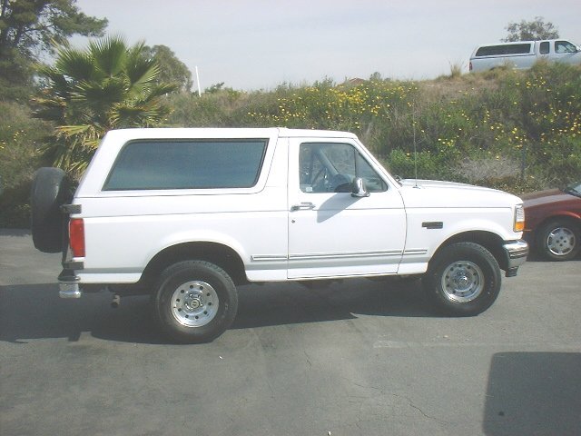 White Ford Bronco profile parked in lot with palm and hillside in background