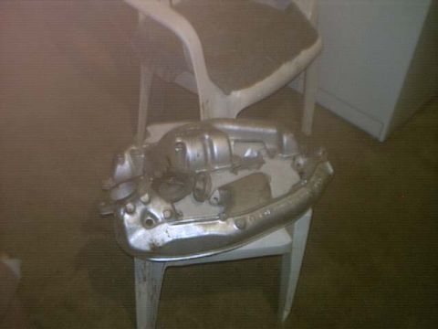 1995 Ford Bronco - A metallic engine part rests on a white chair in a dimly lit room.