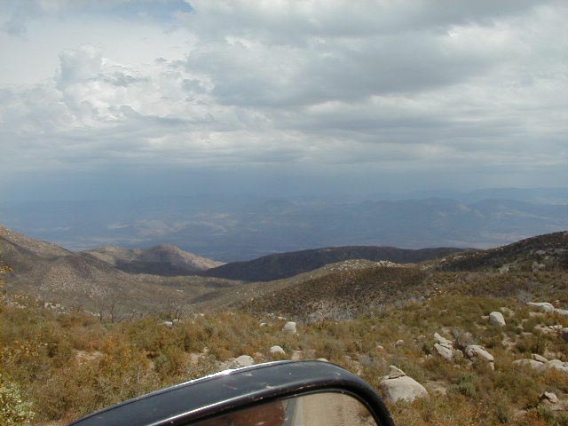 Mountain vista with dark vehicle side mirror in foreground under cloudy sky