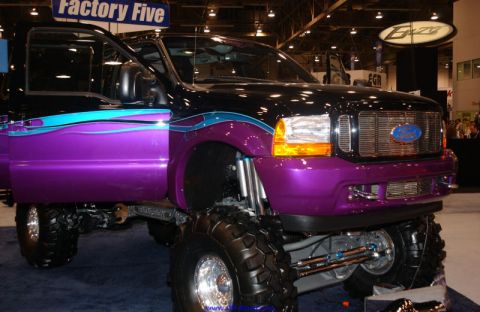 2001 Ford Excursion - This heavily modified Ford truck features a custom paint job and suspension lift, displayed indoors.