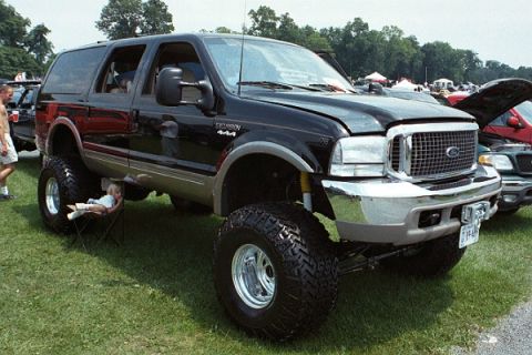 2001 Ford Excursion - A black 2001 Ford Excursion is shown with a lifted suspension and large off-road tires, parked on a grassy field.