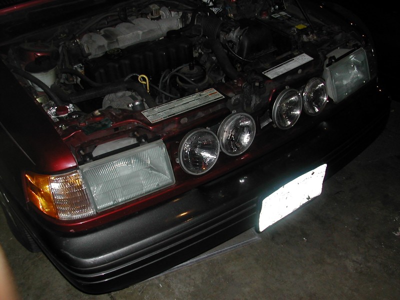 Maroon car front with hood up, loose round headlights on header panel in garage