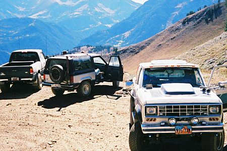 1985 Ford Ranger - Three off-road vehicles are parked on a dirt road with mountains in the background.