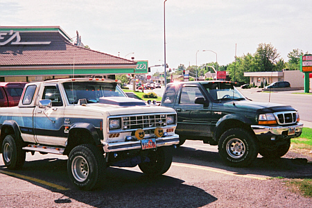 1985 Ford Ranger - A pair of Ford Ranger pickup trucks are parked on a street in front of a building.