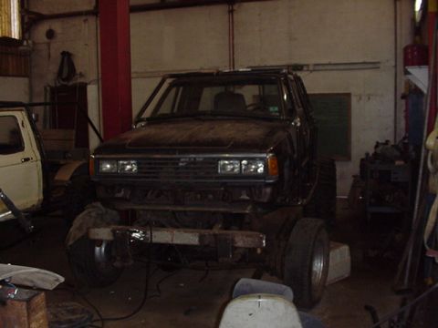 1979 Ford Bronco - A dark, modified SUV sits in a garage, appearing to be undergoing work, with a white vehicle partially visible to its left.