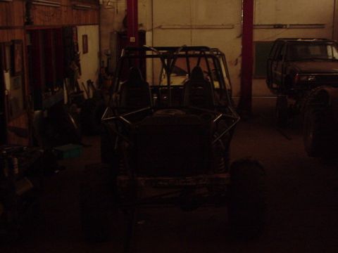1979 Ford Bronco - A custom-built off-road buggy with a prominent roll cage is seen in a workshop, with another vehicle partially visible to the right.