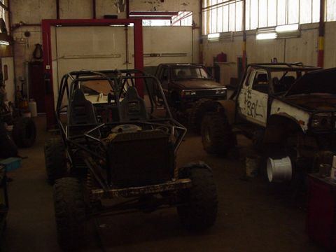 1979 Ford Bronco - Several custom off-road vehicles are parked inside a workshop, some appear to be under construction.
