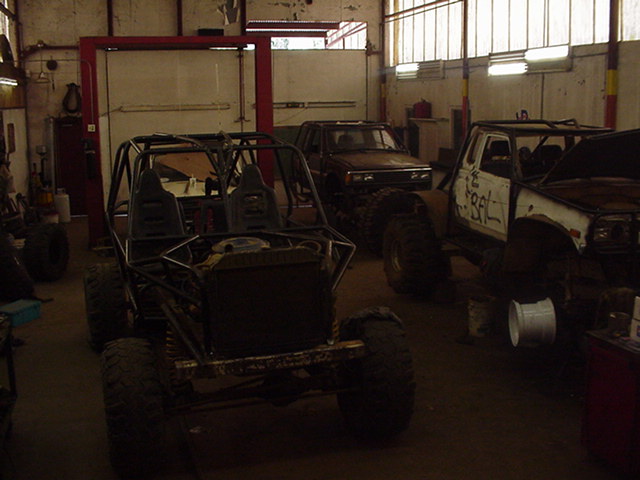 Off-road buggy in foreground, modified trucks in background inside a garage