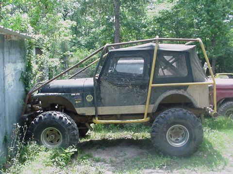 1979 Ford Bronco - A heavily modified Jeep CJ, a roll cage and large tires, is parked close to a concrete structure.