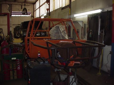 1979 Ford Bronco - A vehicle chassis with an orange roll cage is being worked on in a garage, with other vehicles in the background.