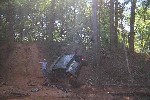 1979 Ford Bronco - A person stands near an off-road vehicle that has slid into a muddy ditch surrounded by trees.
