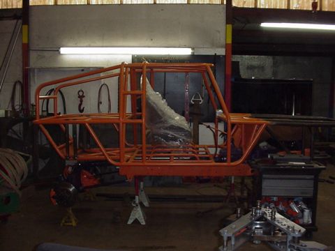 1979 Ford Bronco - Full orange tube chassis for a custom 4x4 buggy under construction on jack stands in a shop, viewed from the driver's side. The welded cage…