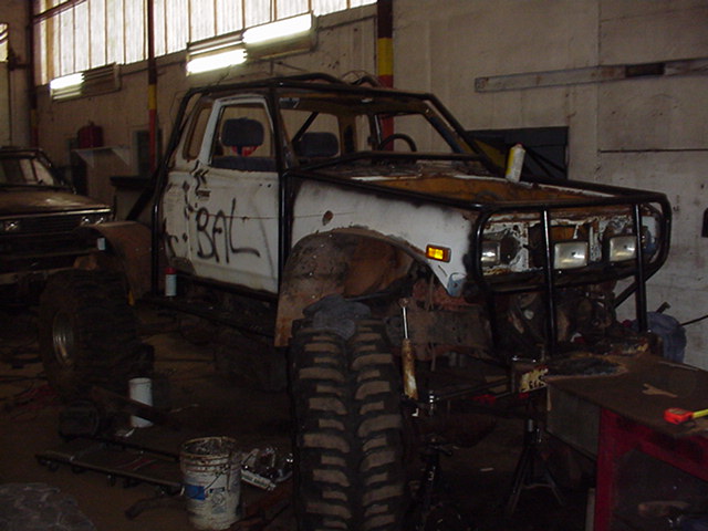 White lifted 4x4 truck body being stripped and rebuilt in a workshop, rusty with roll cage.