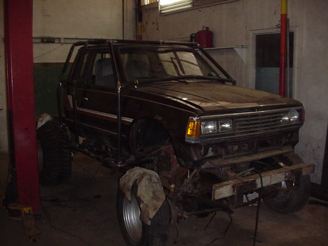 Dark lifted SUV project truck on large tires in a garage, front end partially disassembled