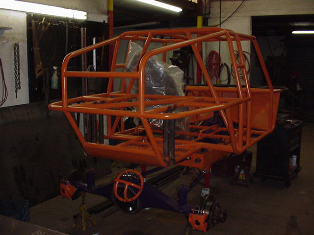 Orange tubular roll cage frame on blue front axle in a workshop