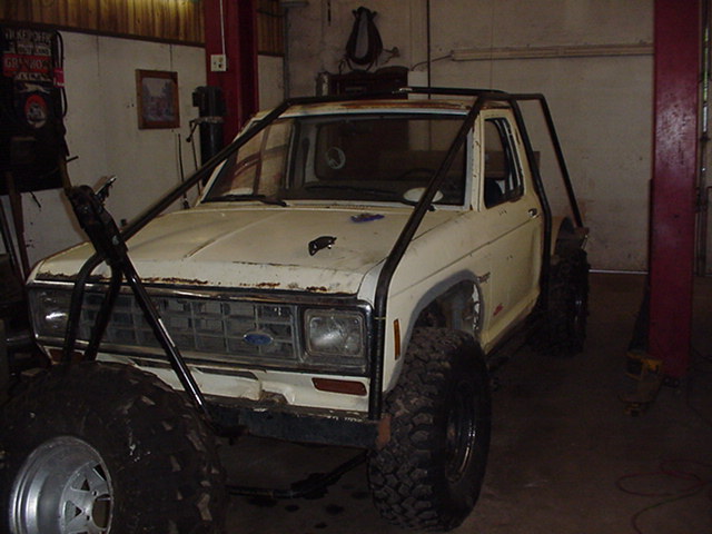 White Ford pickup with roll cage and off-road tires in a garage, under restoration