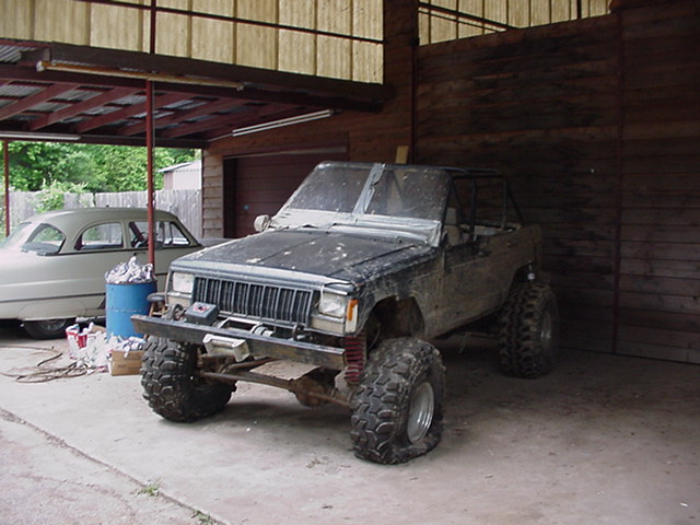 Muddy lifted 4x4 SUV with big off-road tires and winch parked in a wooden barn