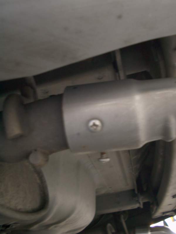 Underbody shot of exhaust pipe with silver heat shield and Phillips screw on a car undercarriage