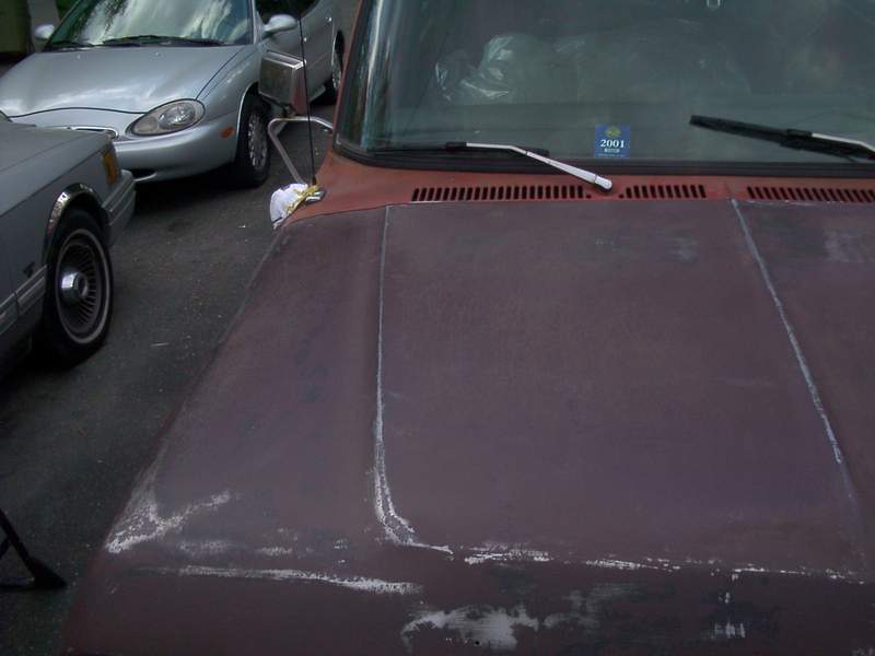 Primer-brown hood and cowl of a truck with 2001 sticker, silver sedan parked alongside