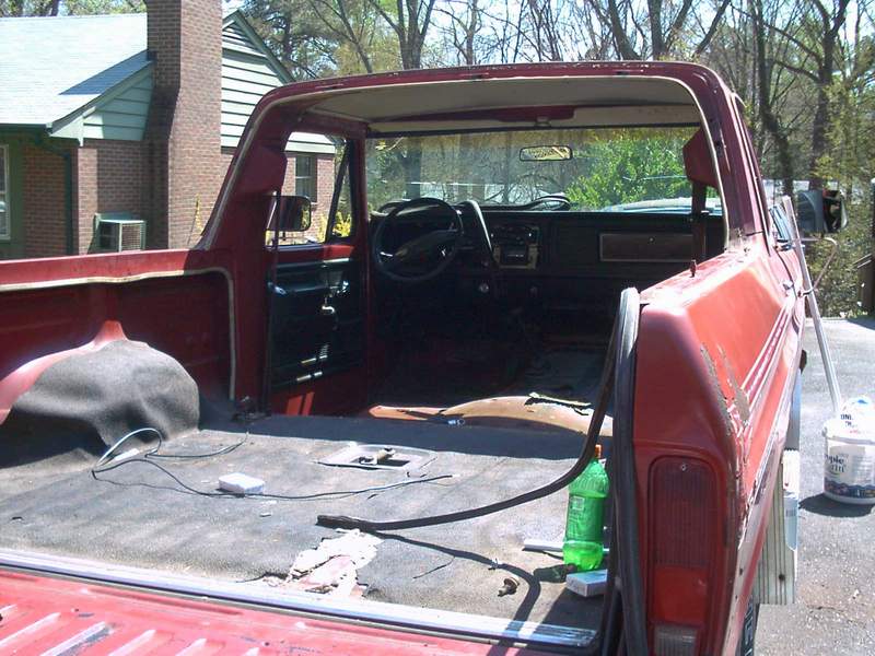Stripped interior of red pickup cab seen through open doors, carpet pulled and dash bare