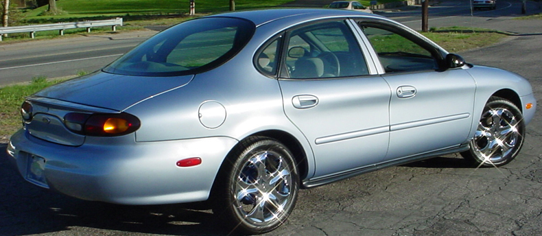 Silver sedan parked on asphalt, rear quarter view. Chrome wheels visible