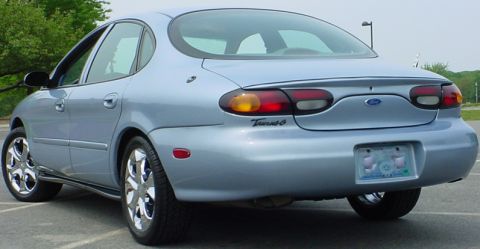 1998 Ford Taurus - The rear end of a light blue 1998 Ford Taurus sedan is shown, its distinctive taillights and chrome wheels.