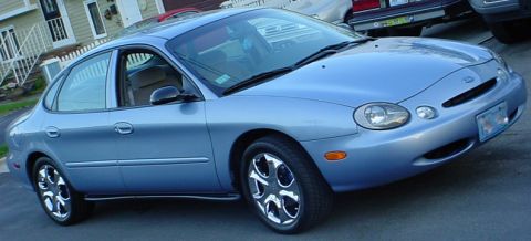 1998 Ford Taurus - A blue 1998 Ford Taurus is shown from a 3/4 front angle, parked in front of a house.