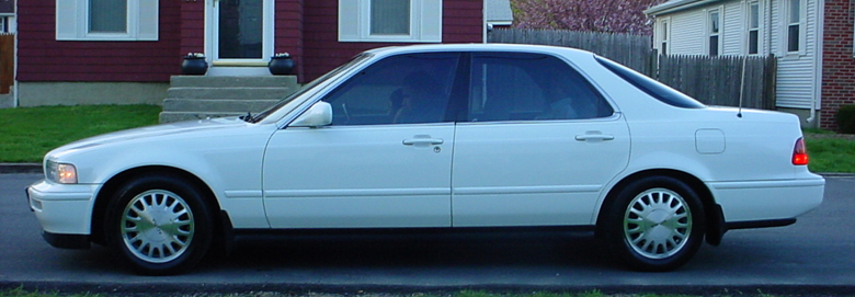 White four-door sedan in side profile parked on street before a dark red house