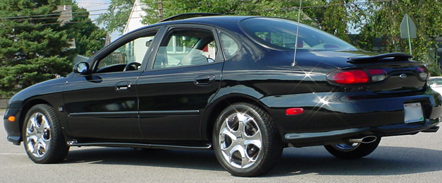 Black Ford Taurus sedan rear three-quarter on chrome wheels with spoiler