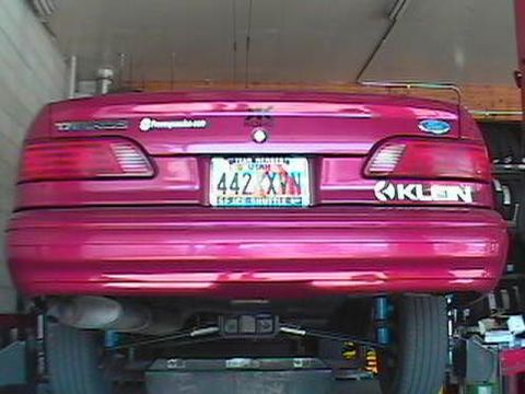 1995 Ford Taurus - The rear of a pink 1995 Ford Taurus is shown, its license plate and a "KLEN" sticker.