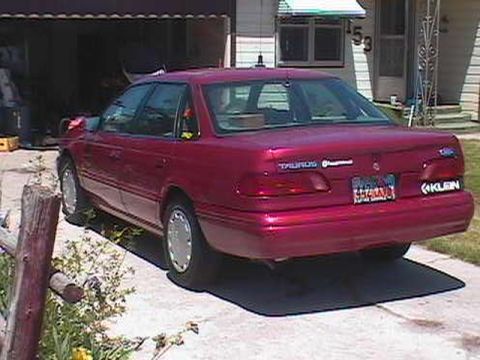 1995 Ford Taurus - The rear of a red 1995 Ford Taurus is visible, parked in front of a garage with a license plate and model badging clearly displayed.