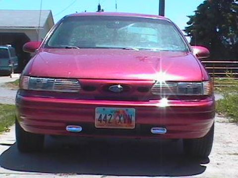 1995 Ford Taurus - This red 1995 Ford Taurus is parked outside a garage on a sunny day.