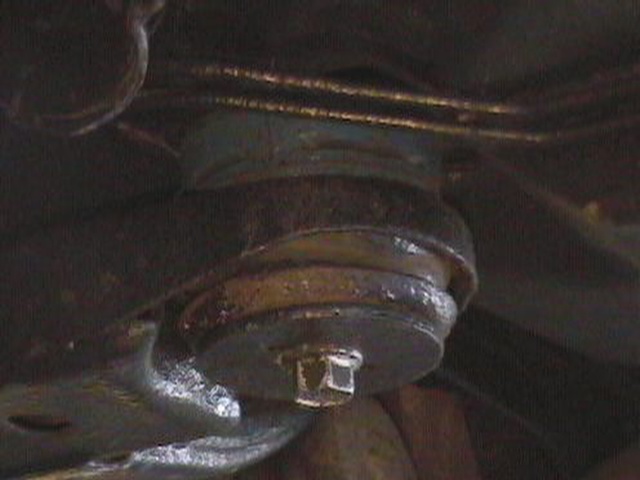 Underside view of a dark, greasy suspension part with a bolt head visible
