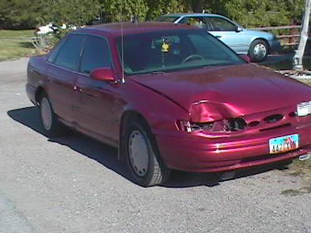 Magenta Ford Taurus sedan with front collision damage to bumper