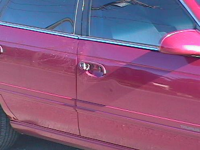 Dented passenger-side door with scrapes on a dark red Ford Taurus