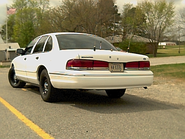 White Ford Crown Victoria ex-police sedan, rear three-quarter view with trunk-mounted antennas