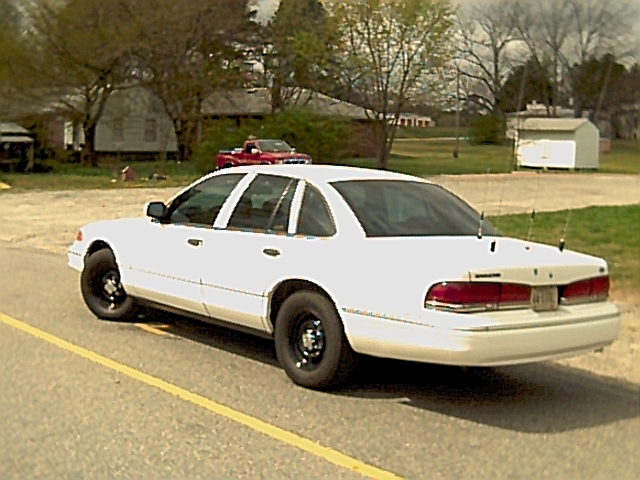 White Ford Crown Victoria ex-police sedan on black steel wheels with trunk antennas