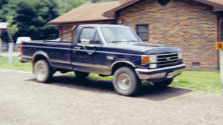 1990 Ford F-150 - A dark blue 1990 Ford F-150 pickup truck is parked outside a brick building.