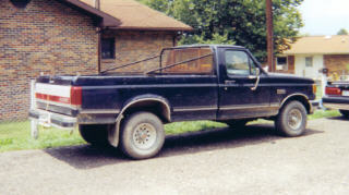 1990 Ford F-150 - This 1990 Ford F-150 pickup truck is seen from the side, an aftermarket bed rack and a dark blue paint job.