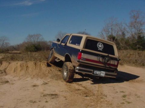 1990 Ford Bronco - This Ford Bronco is navigating a sandy, off-road terrain under a clear blue sky.