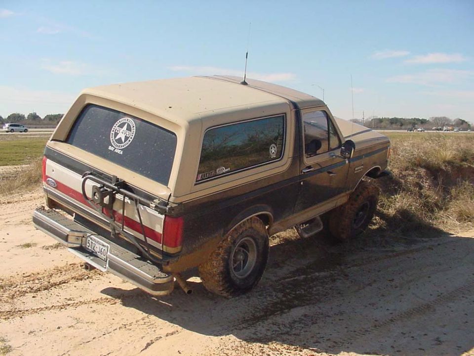 Tan and brown Ford Bronco SUV, rear 3/4 view, stuck in sand with muddy tires