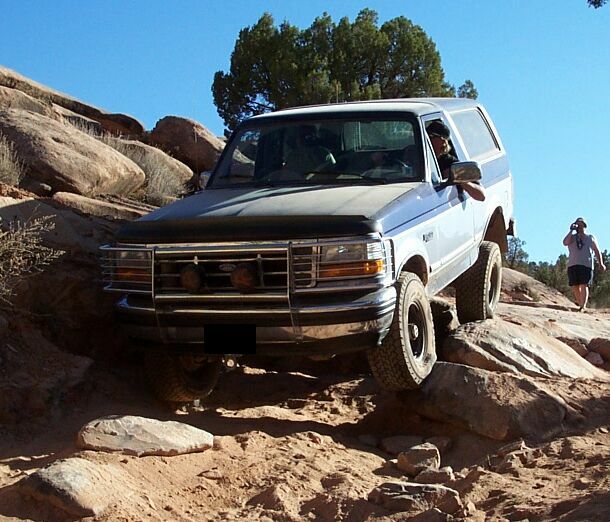 1994 Ford Bronco navigating a rocky trail with a person walking in the background
