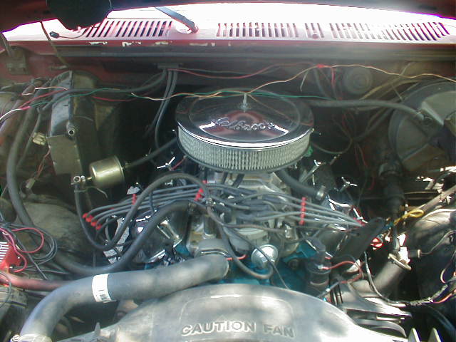 Engine bay with V8, chrome Edelbrock air cleaner, red plug wires, and fan shroud marked CAUTION FAN