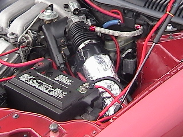 Red Ford Taurus engine bay with foil-wrapped intake tube, red plug wires, braided hose, and battery