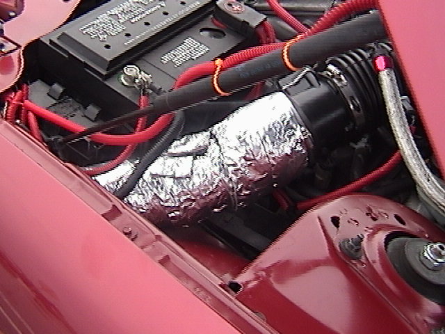 Engine bay with foil-wrapped intake tube, battery, red wiring, and strut tower on a red car