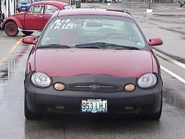 Front of maroon Ford Taurus with black bra and amber fog lights in wet lot