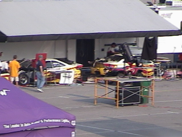 Race cars parked under a canopy, one yellow and white, another with red and yellow flames