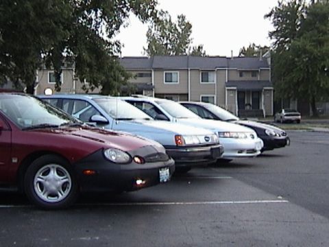 1998 Ford Taurus - Several cars are parked in a lot, with a red Ford Taurus in the foreground.