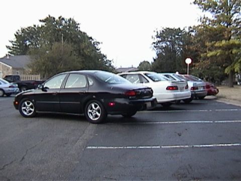 1998 Ford Taurus - Several sedans are parked in a lot, including a black 1998 Ford Taurus.