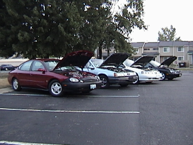 Maroon Ford Taurus with hood open, parked in a lot with other cars